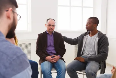Group therapy session with man placing hand on another's shoulder